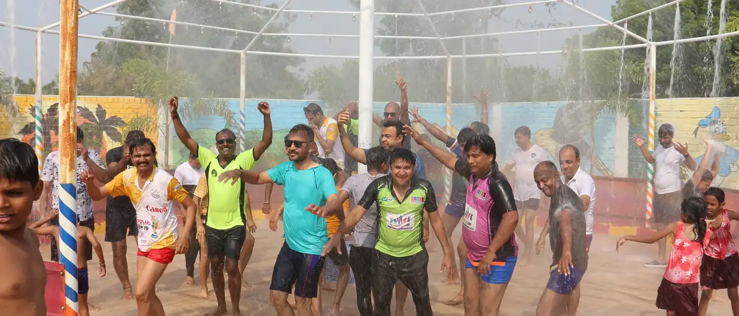 A wide view of families playing under the sprinklers, arms up in the falling water